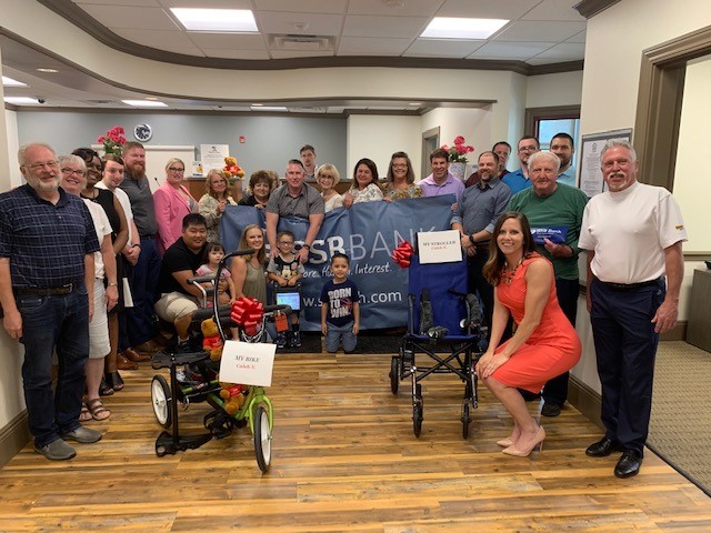 ssb bank staff presenting recumbent bike, stroller and communication device with variety the childrens charity